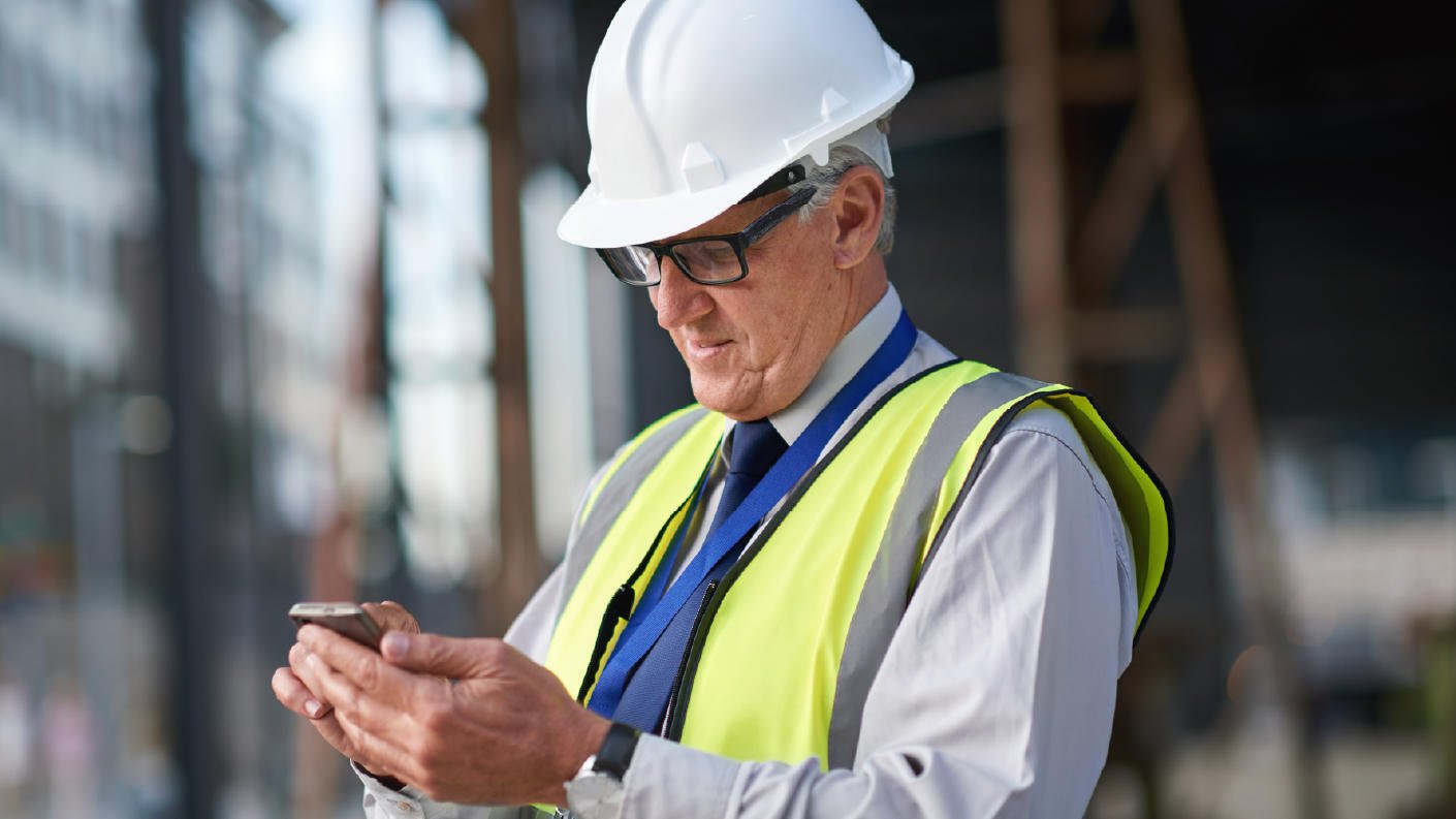 Construction worker with a white hard hat and yellow vest looking at his phone